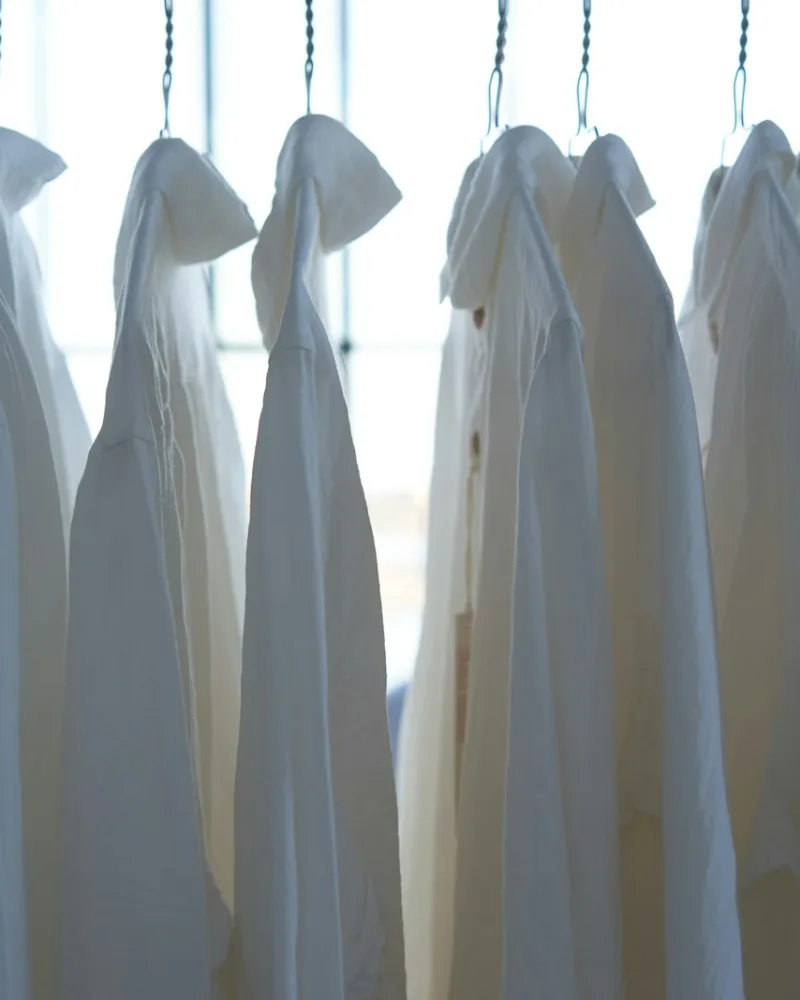 Camisas e jalecos brancos pendurados em cabides, contra a luz