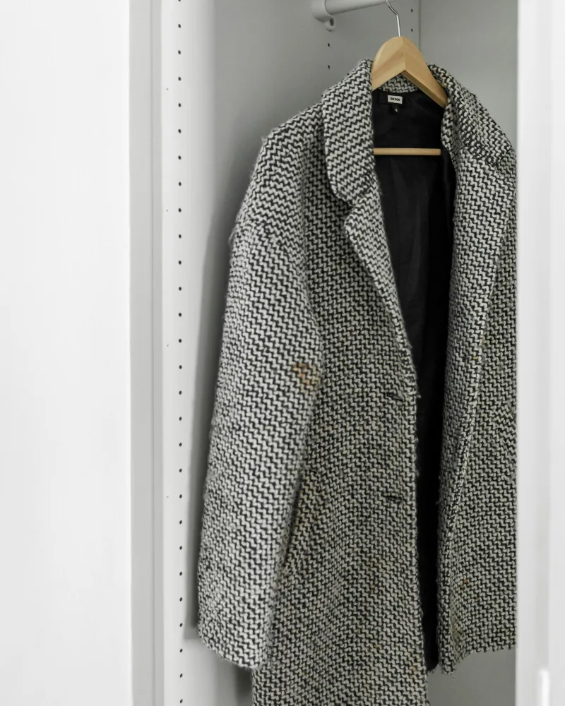 Casaco de tweed preto e branco pendurado num cabide, dentro de um armário branco