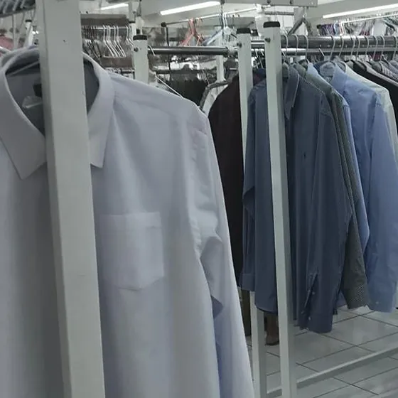 Camisa social clara passada, no cabide, e araras de camisas prontas para entrega na Dedicada Lavanderia