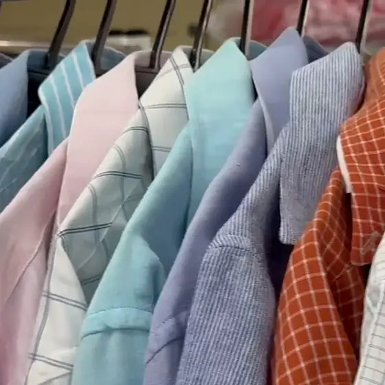 Camisas sociais coloridas lavadas e passadas, penduradas em cabides na Dedicada Lavanderia