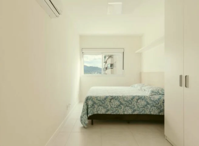Suíte de apartamento de temporada com cama queen arrumada com colcha estampada e lençóis lavados pela Dedicada Lavanderia