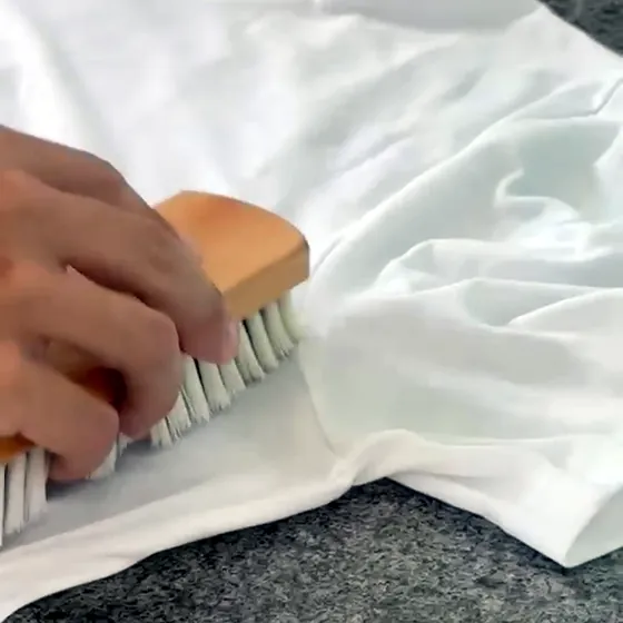 Mão esfregando com escova um tecido branco sobre a bancada de pré-tratamento da Dedicada Lavanderia
