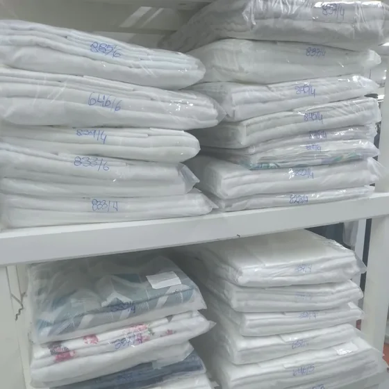 Prateleira com jogos de lençóis lavados e passados, embalados um a um em sacos plásticos e identificados à mão, na Dedicada Lavanderia