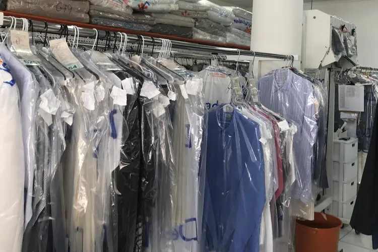 Araras com camisas e outras peças prontas, no cabide e em sacos plásticos, com etiquetas de identificação, na produção da Dedicada Lavanderia