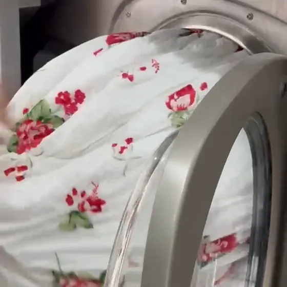 Roupa de cama estampada com rosas sendo retirada de uma lavadora industrial na Dedicada Lavanderia