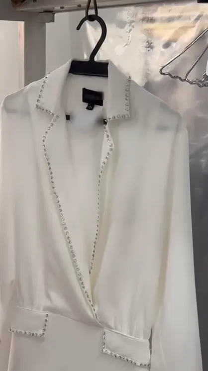 Vestido branco de manga longa com pedraria na gola, no decote e na cintura, passado e pendurado no cabide, na Dedicada Lavanderia