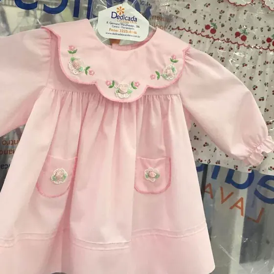 Vestido de bebê rosa com gola bordada, no cabide com a etiqueta da Dedicada Lavanderia