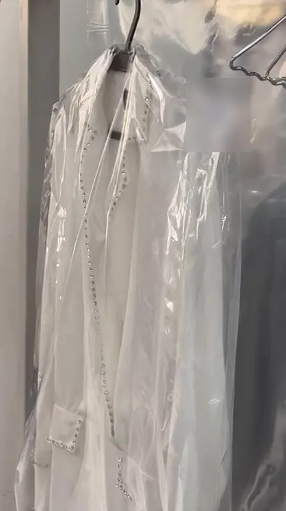 O mesmo vestido branco com pedraria, no cabide e embalado em plástico, pronto para voltar à cliente