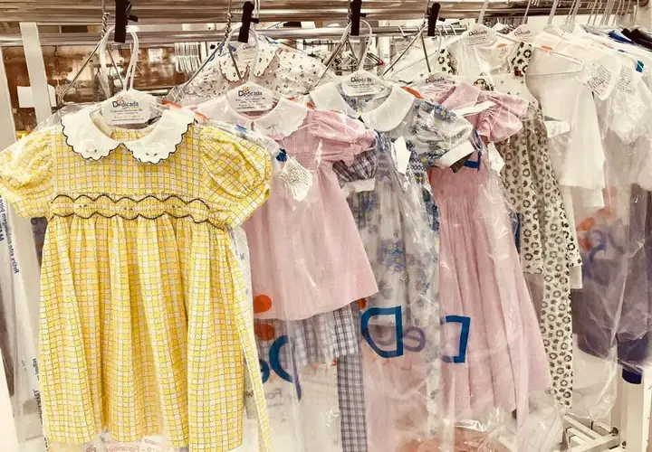Vestidos infantis com bordado e casinha de abelha, lavados e passados, nos cabides da Dedicada Lavanderia