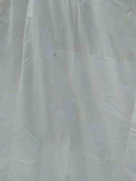 Detalhe de edredom branco antes da lavagem, com uma mancha pequena e áreas amareladas