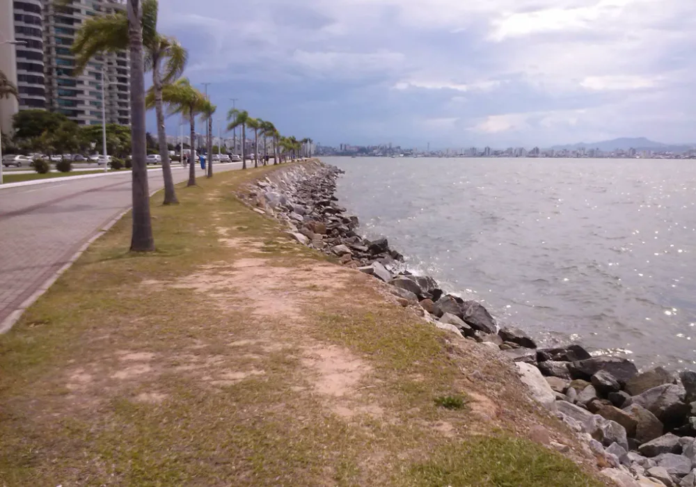 A orla da Beira-Mar Norte, com palmeiras, a calçada e as pedras junto ao mar, em Florianópolis