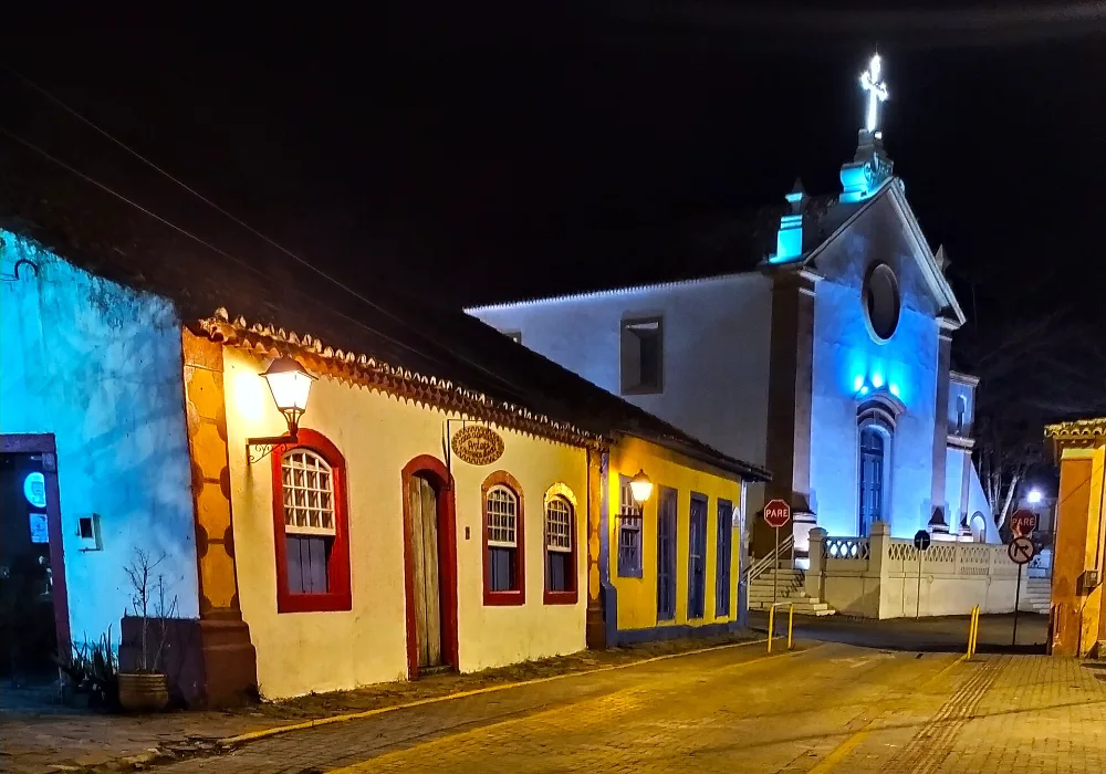 Casario colorido e a Igreja de Nossa Senhora das Necessidades iluminados à noite, no centrinho de Santo Antônio de Lisboa, em Florianópolis