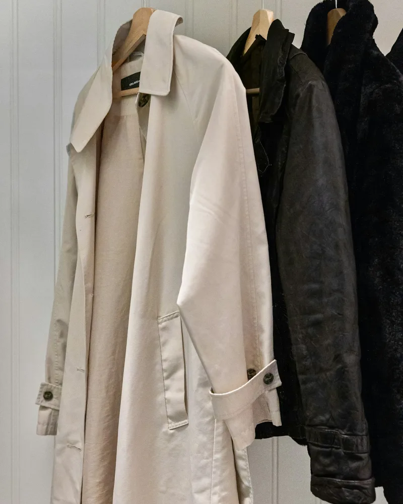 Trench coat bege e casacos pretos pendurados num cabideiro