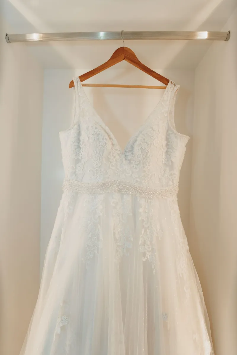 Vestido de noiva branco de renda, pendurado num cabide de madeira dentro de um armário